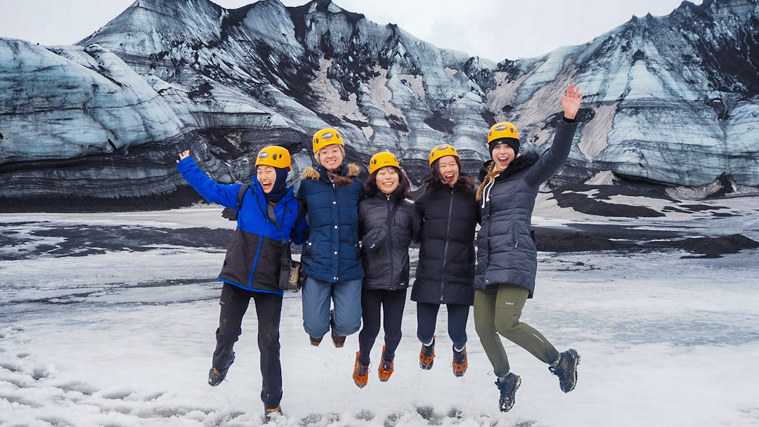 a group jumps in the air with snow-capped mountains in the background