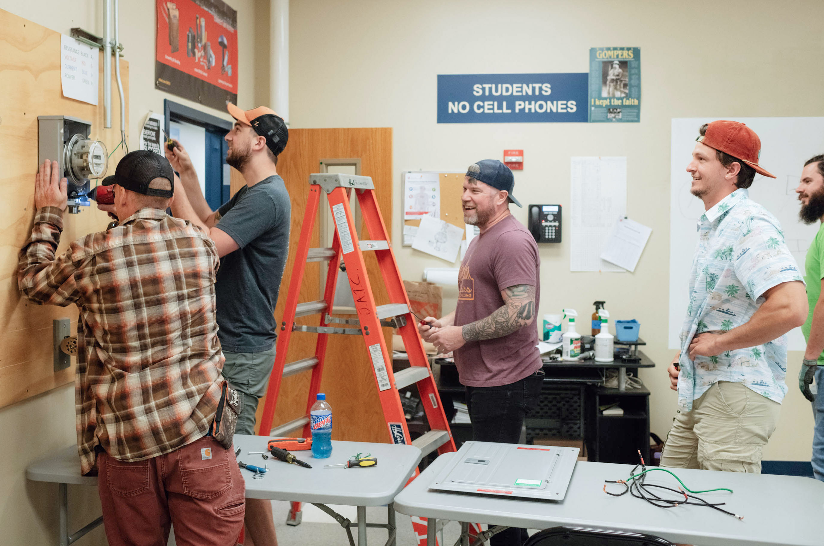 Un grupo de 5 hombres trabajan instalando un medidor eléctrico en un salón de clases.