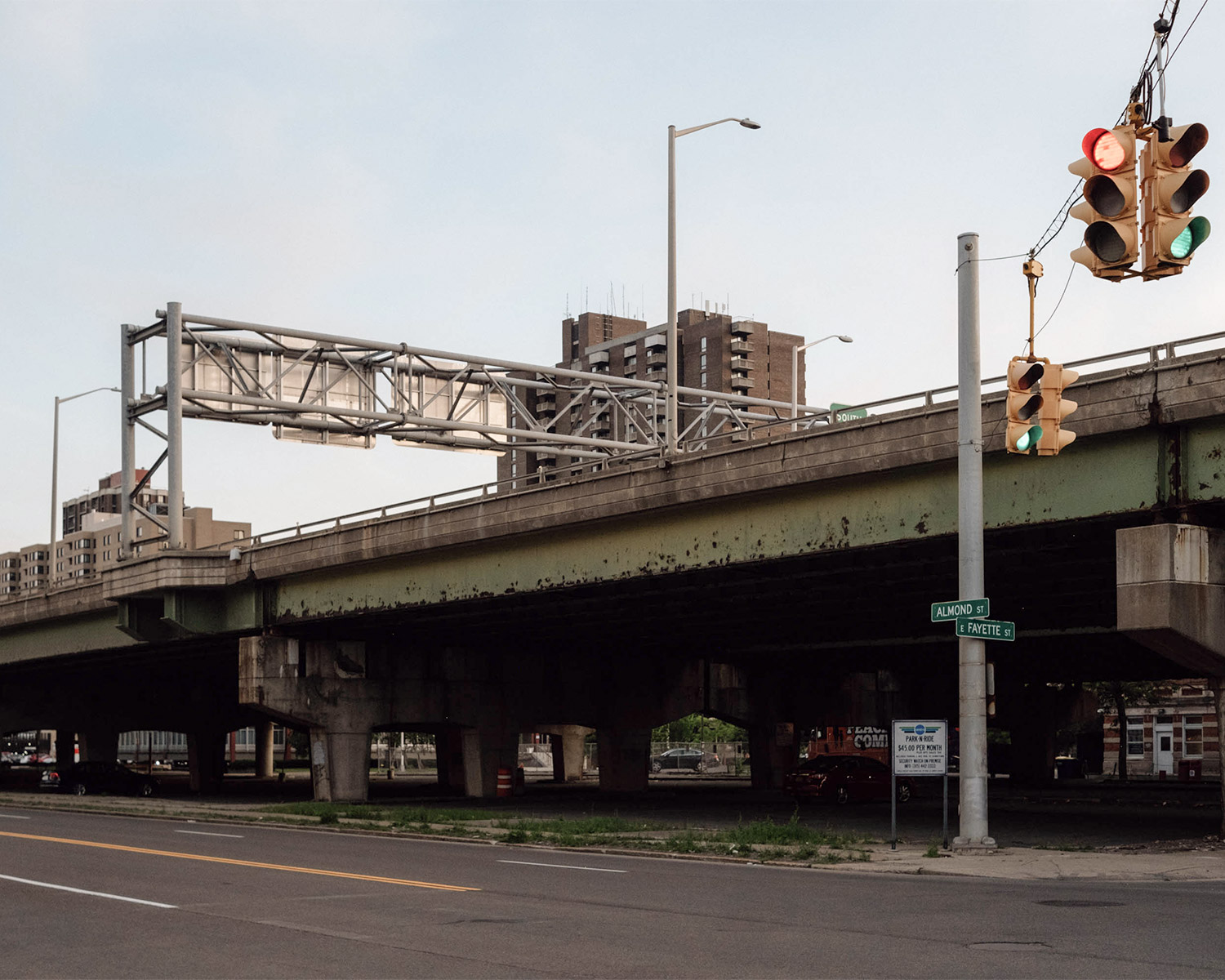 An industrial street scene showing a rusty overpass with traffic lights in the foreground.