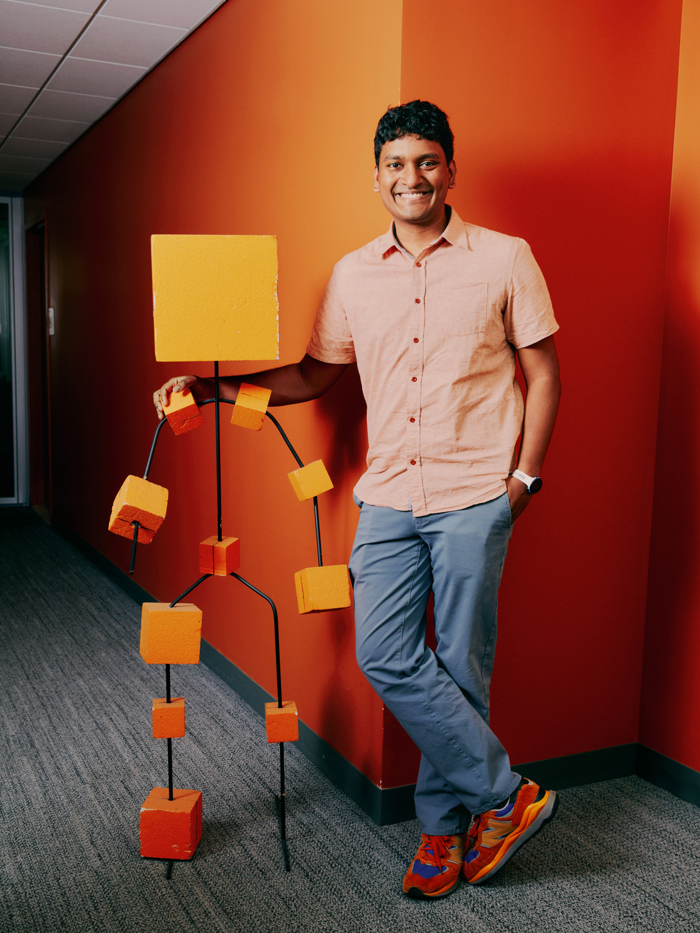Lerrel Pinto standing next to a anthropomorphic model made of orange blocks