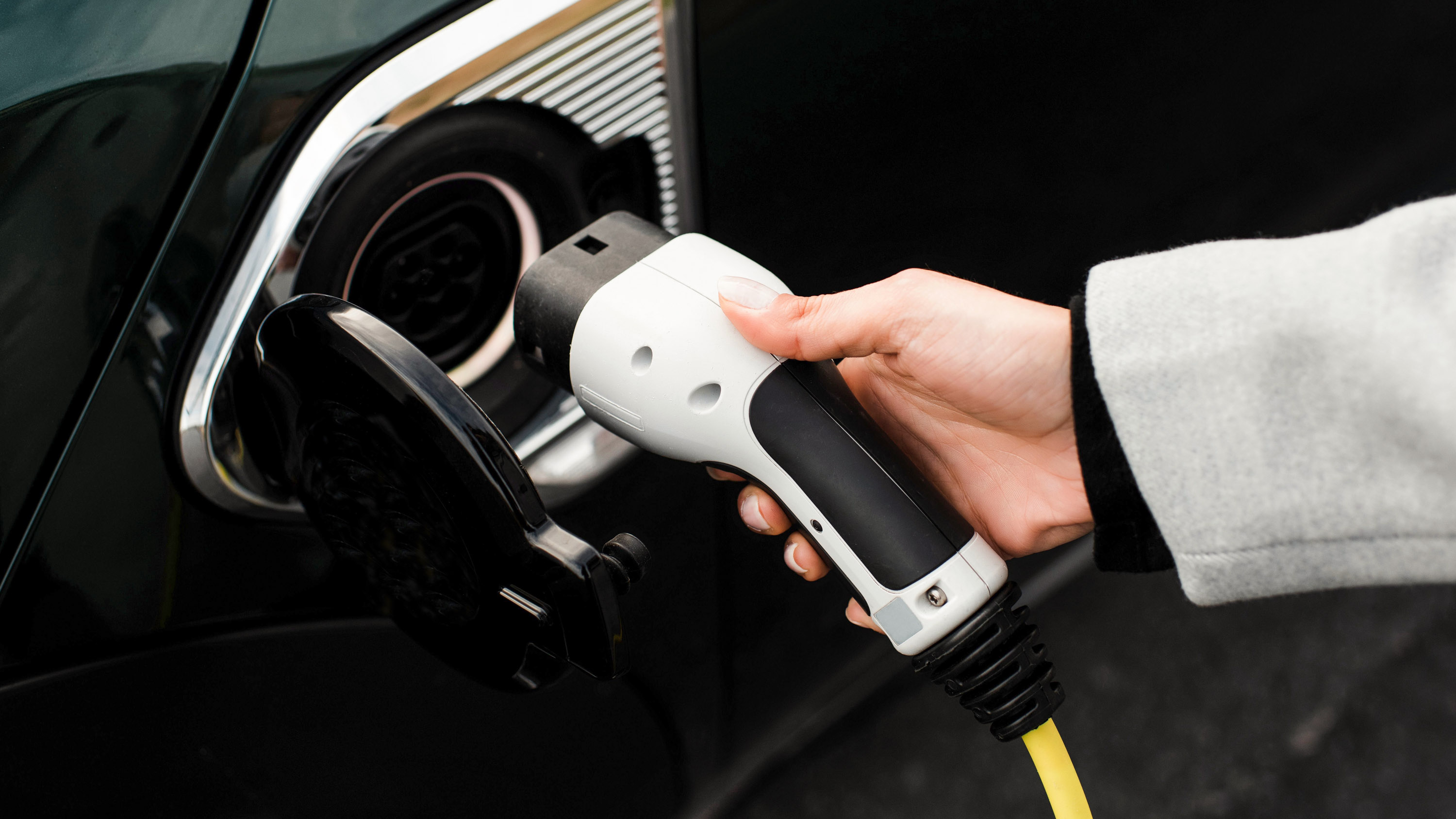 woman&#039;s hand plugging in a charger to an electric car socket
