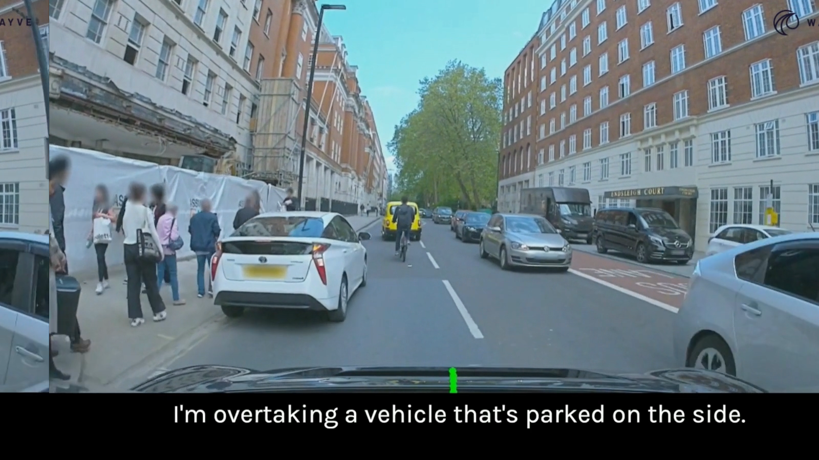 through the windshield shot of a driverless car with the AI narration of its driving performance in caption at the bottom reading, &quot;I&#039;m overtaking a vehicle that&#039;s parked on the side.&quot;
