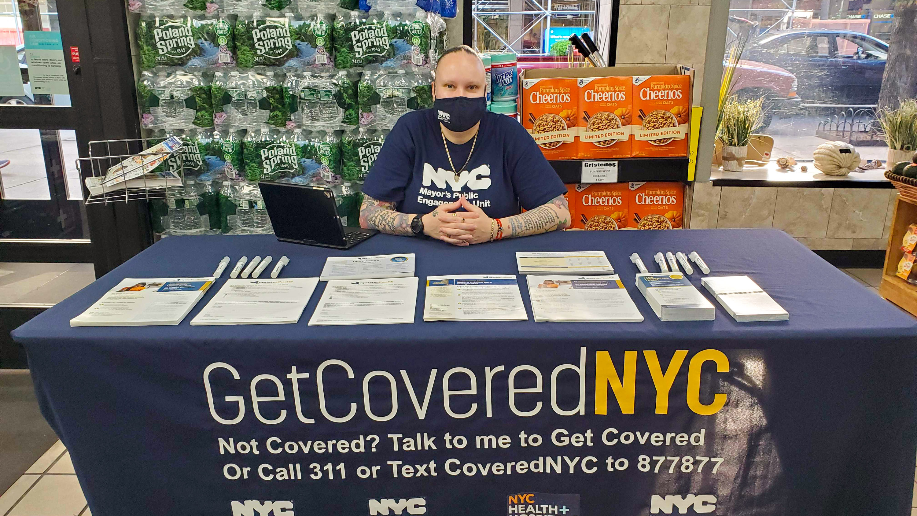 Jessica Ramgoolam sitting at a table with forms and a runner that reads &quot;Get Covered NYC&quot;