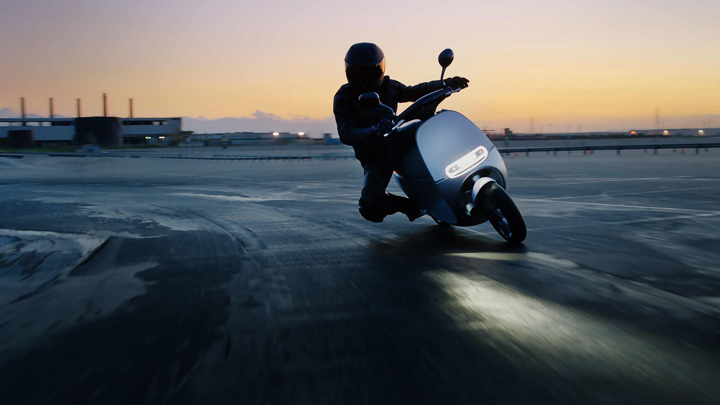 a helmeted Gogoro rider leans to make a turn at sunset