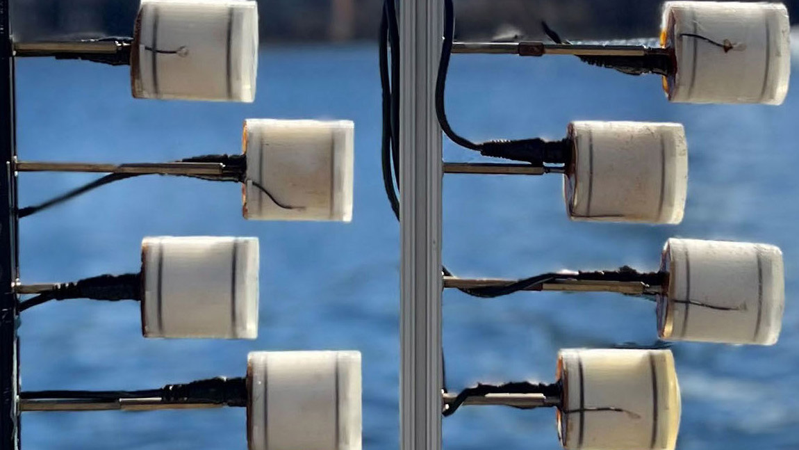 Eight piezoelectric transducers look like toilet paper rolls and are attached to poles, near water.
