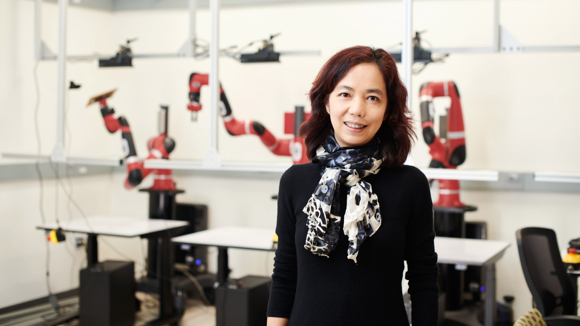 Fei-Fei Li standing in front of several red robot arms