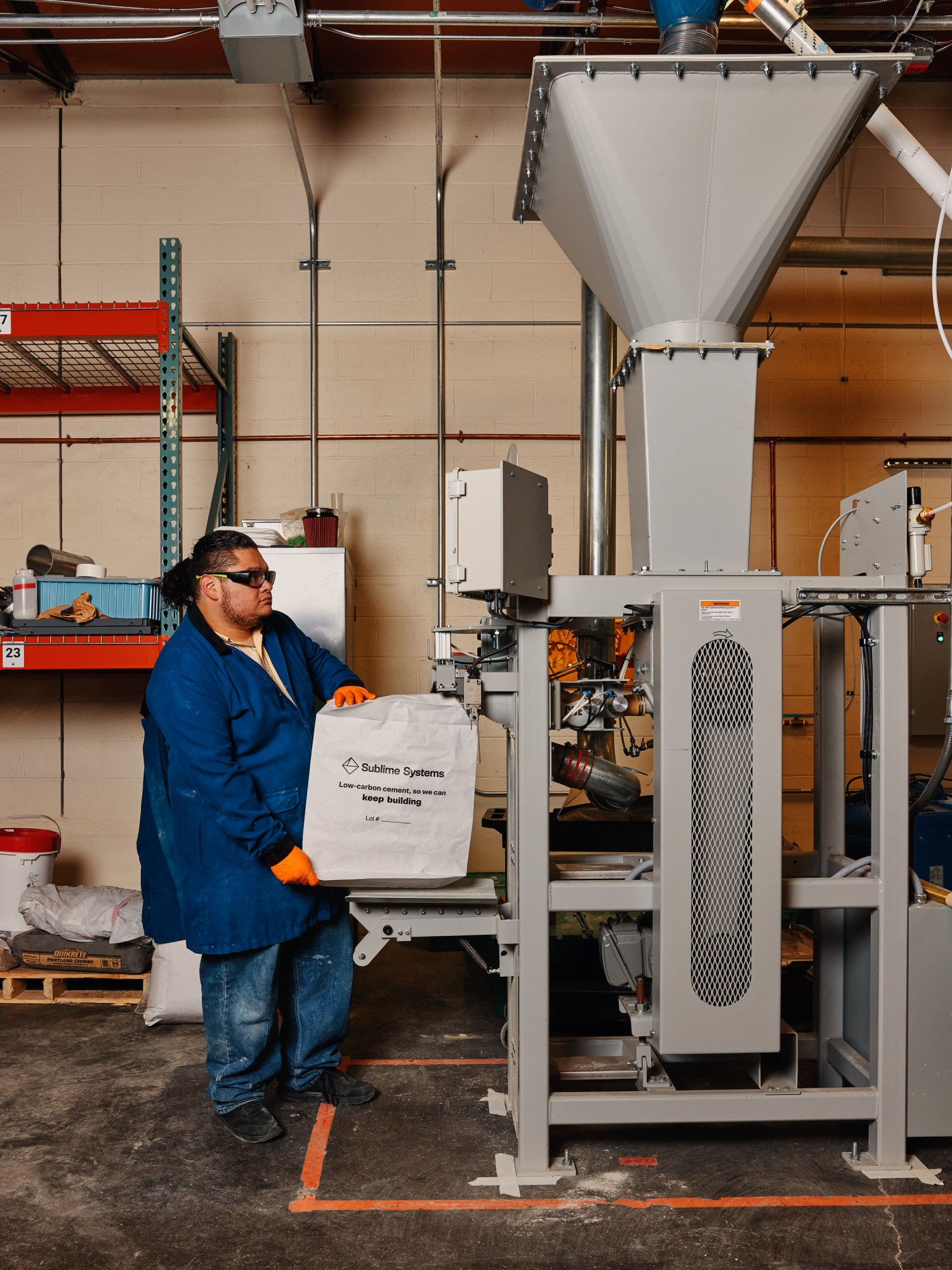 A worker loading a bag that reads " Sublime Systems; Low-carbon cement, so we can keep building" into a large machine