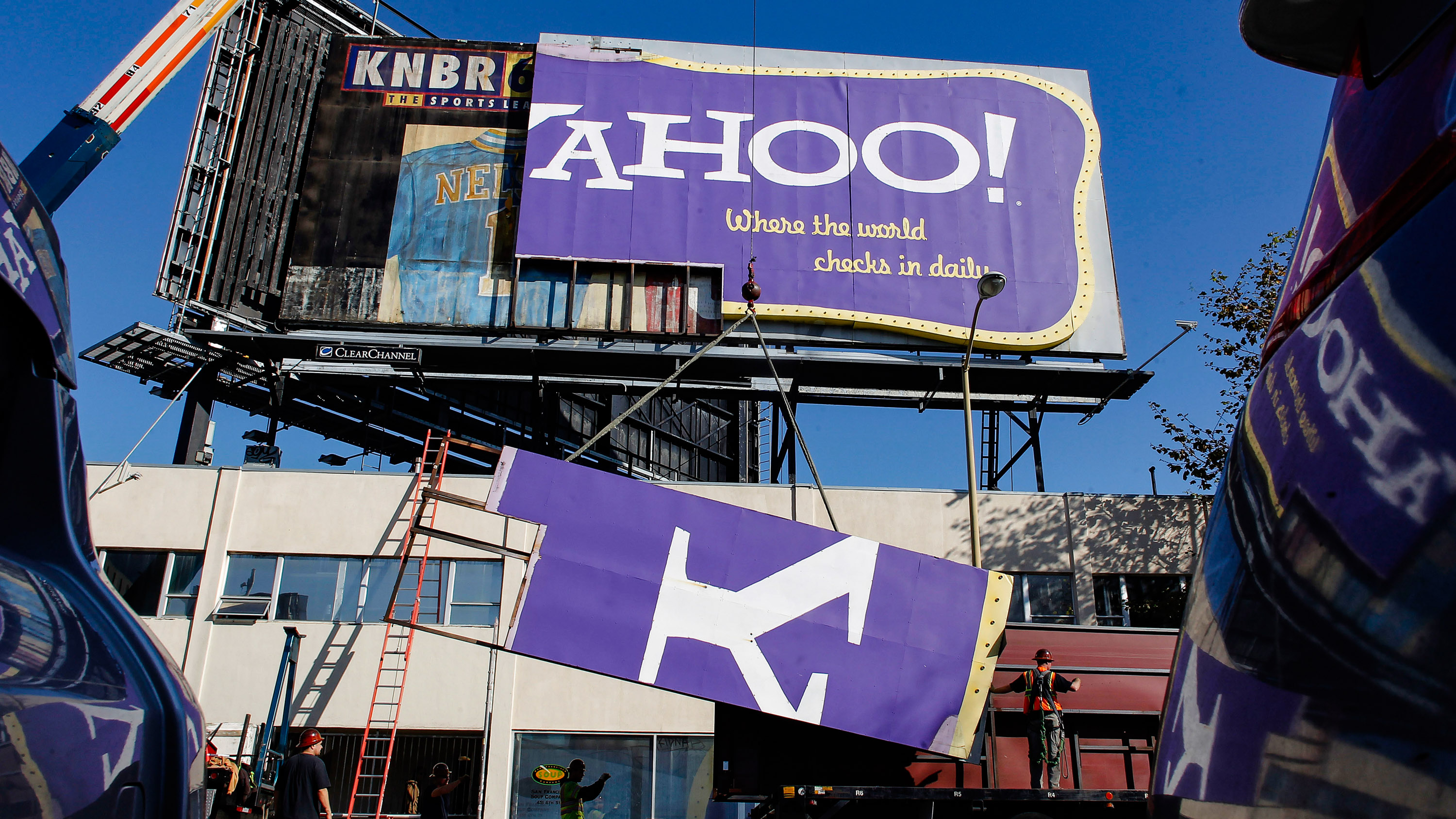 seen from between parked cars, workers with hard hats and ladders are taking down the Y of an old Yahoo! billboard
