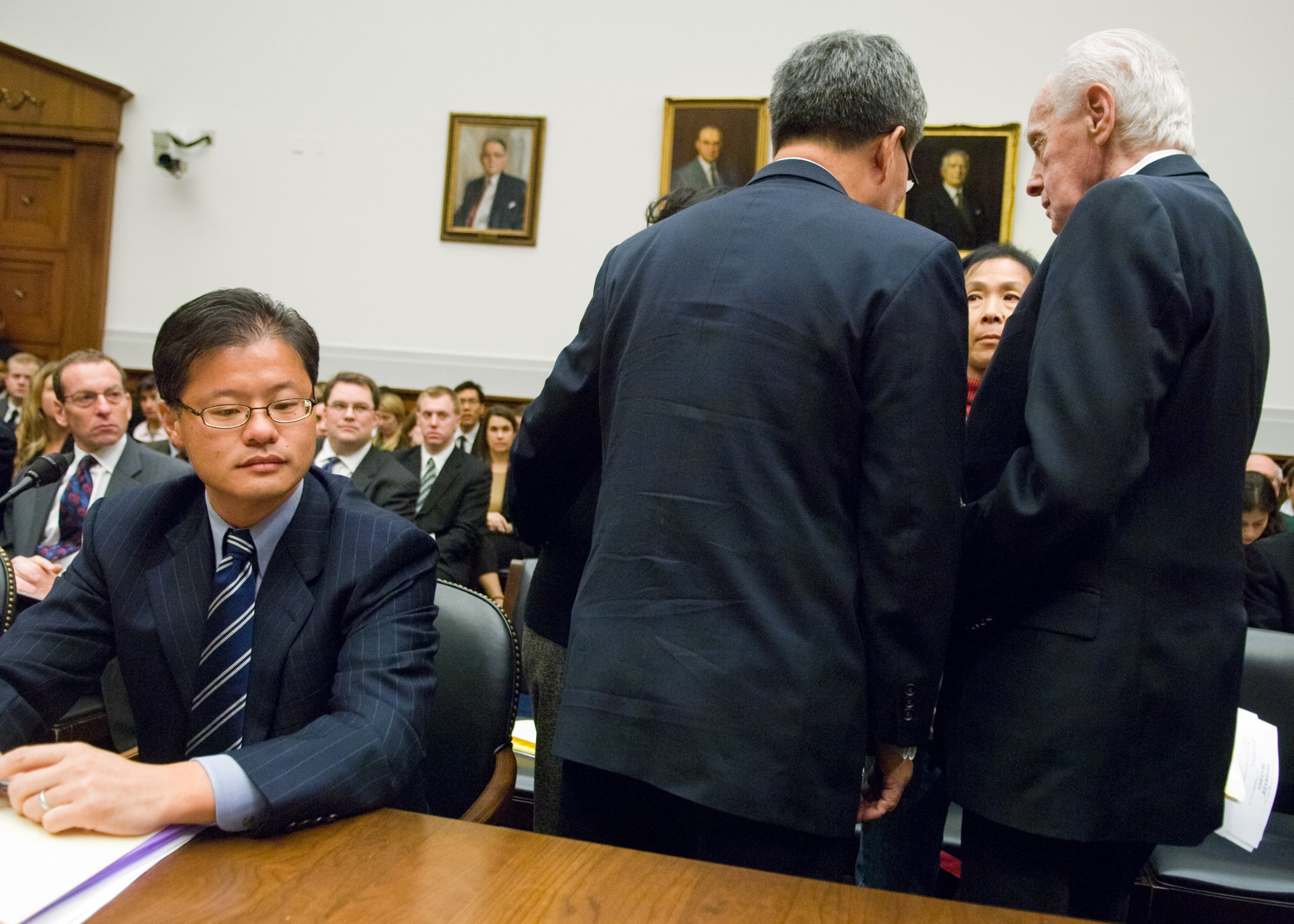 Jerry Yang seated to the left while the backs of Tom Lantos and Harry Wu are to camera as they stand with Yu Ling