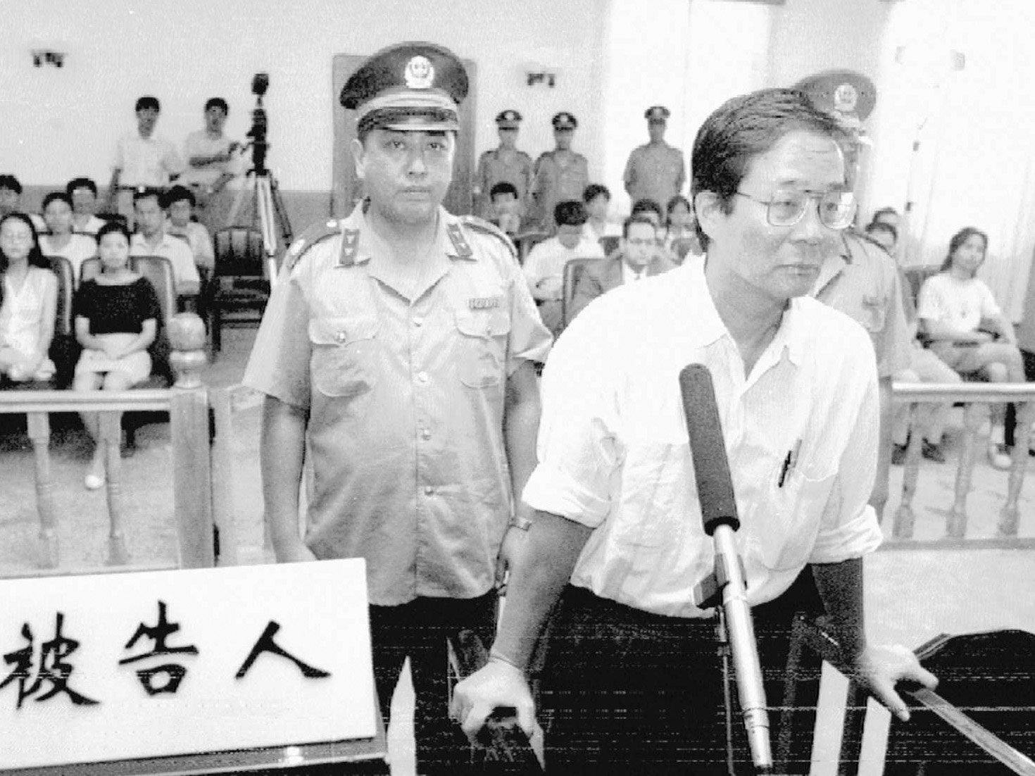 black and white image of Harry Wu at trial with a court officer looking at camera