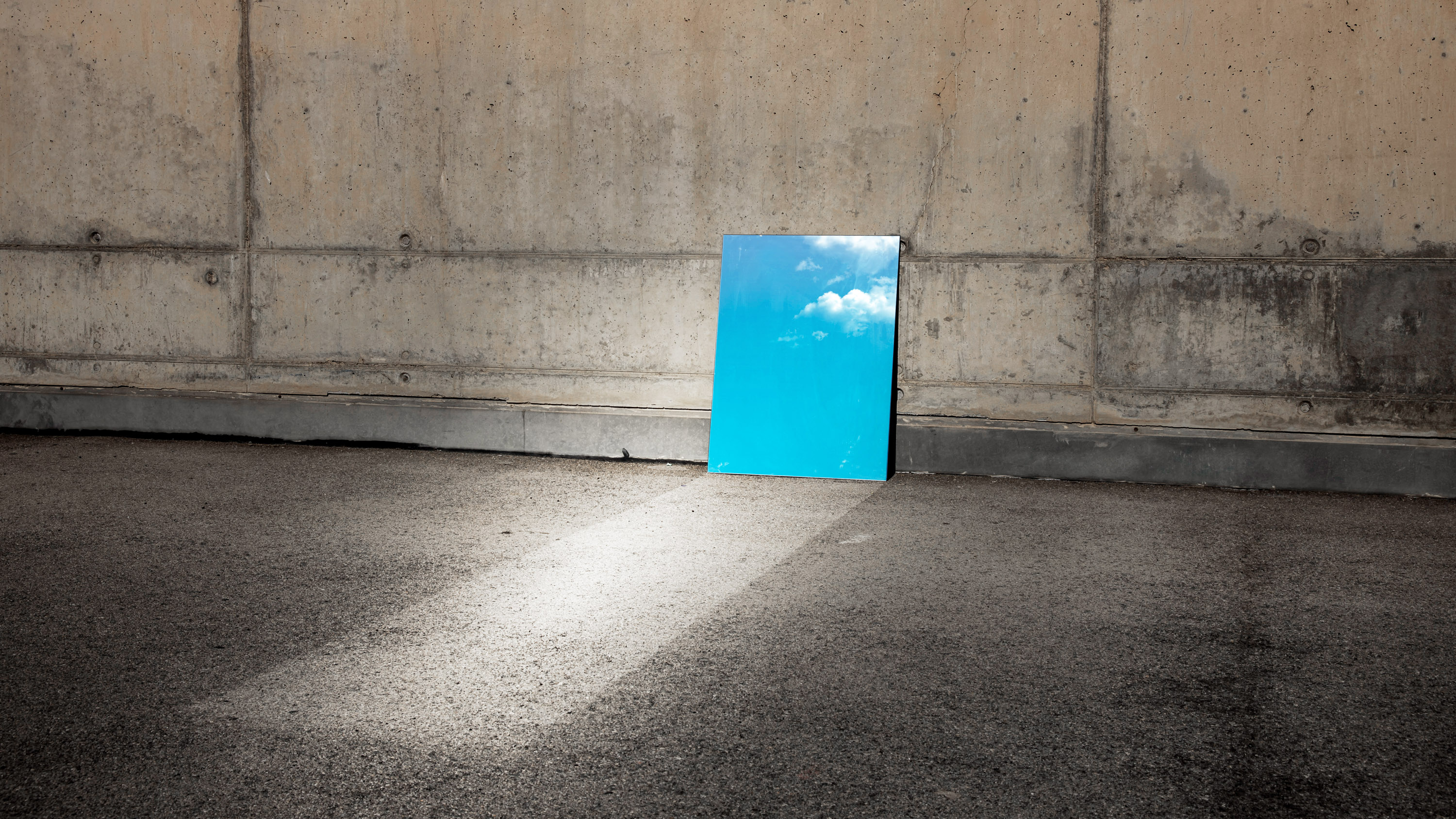 a mirror resting against a concrete wall reflects skylight onto the pavement