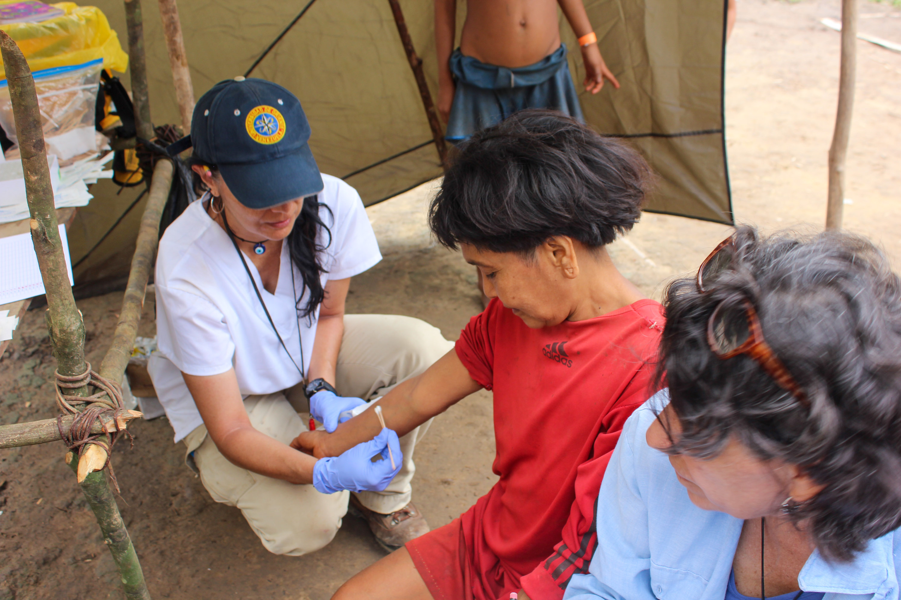 a person in a baseball cap collects a swab from the skin of Yarima while another researcher watches