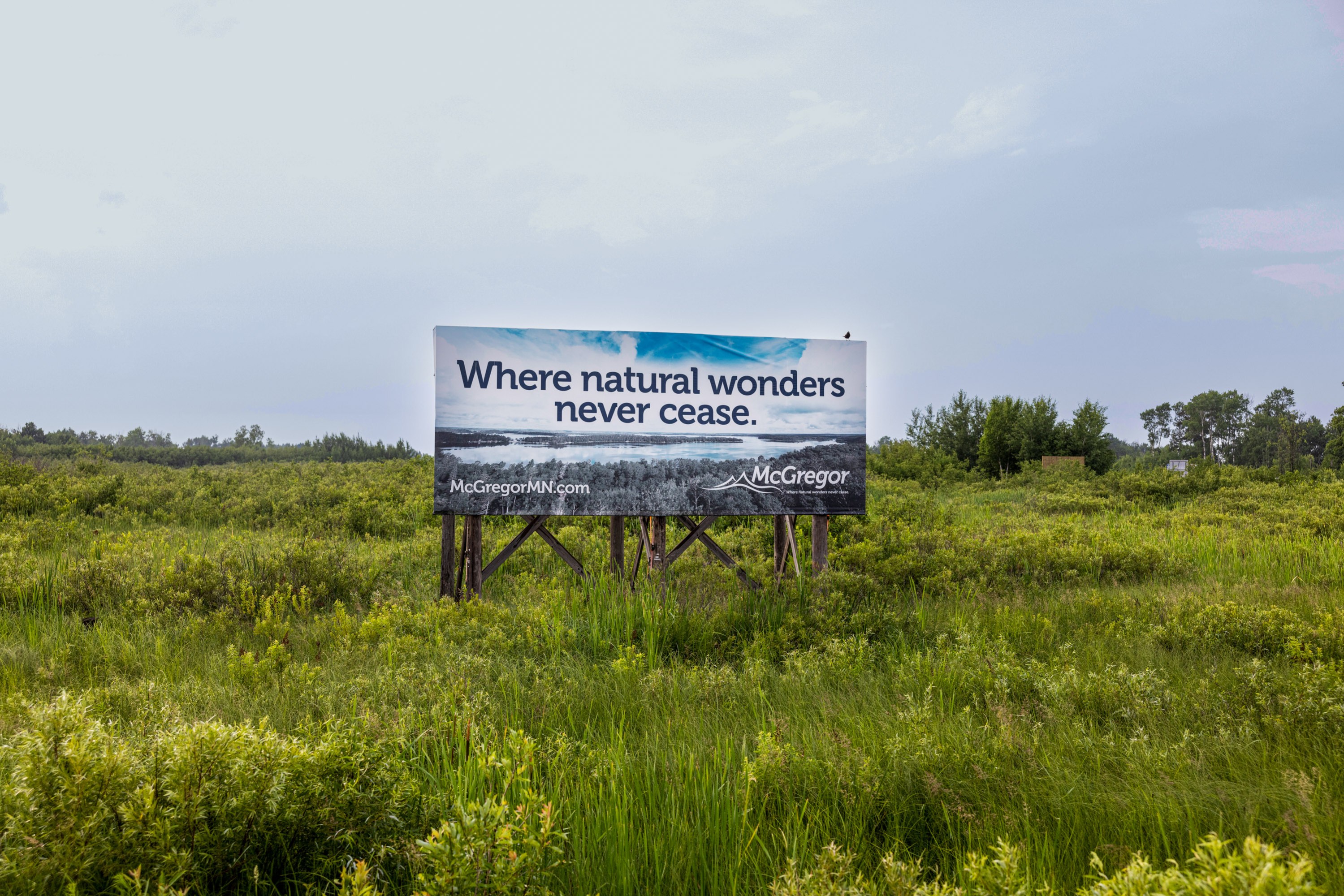 A billboard in a grassy field that reads, "Where natural wonders never cease. McGregor MN"