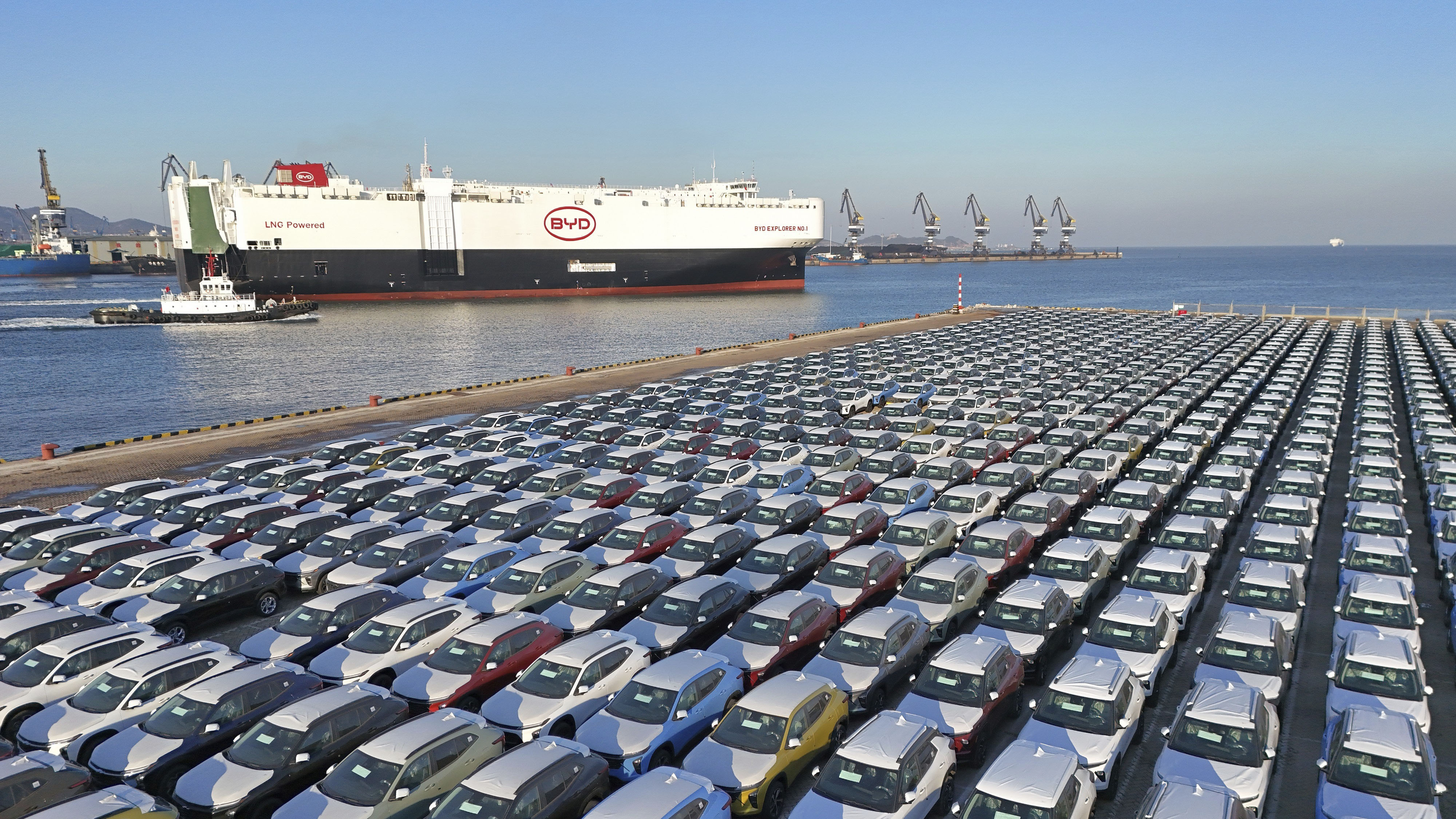 Thousands of cars are shown on a car carrier on a seaport, with a BYD freight boat in the background.