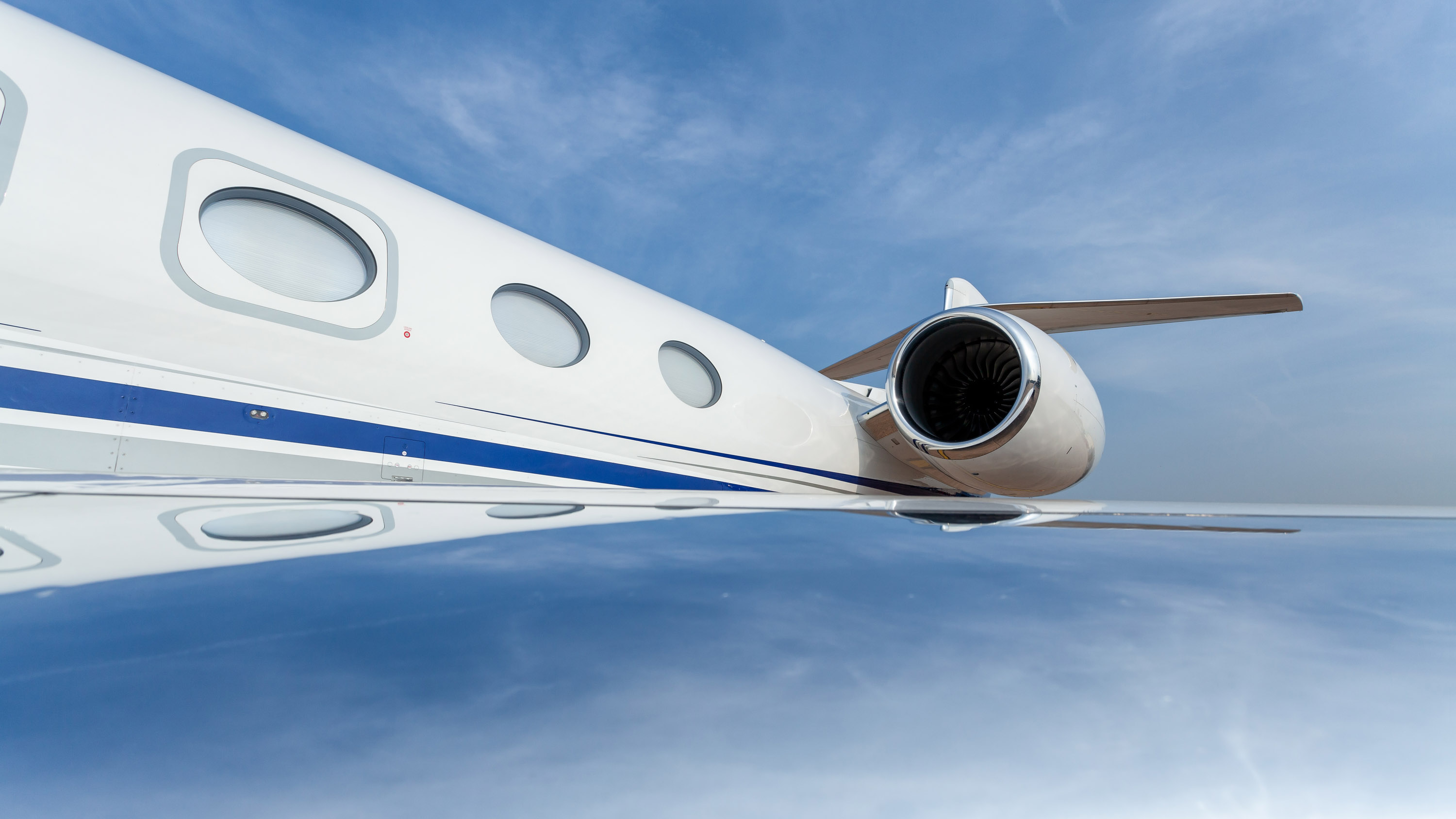 A Gulfstream G650 private jet. Wide angle view of the fuselage, wing and engine with blue sky reflections.