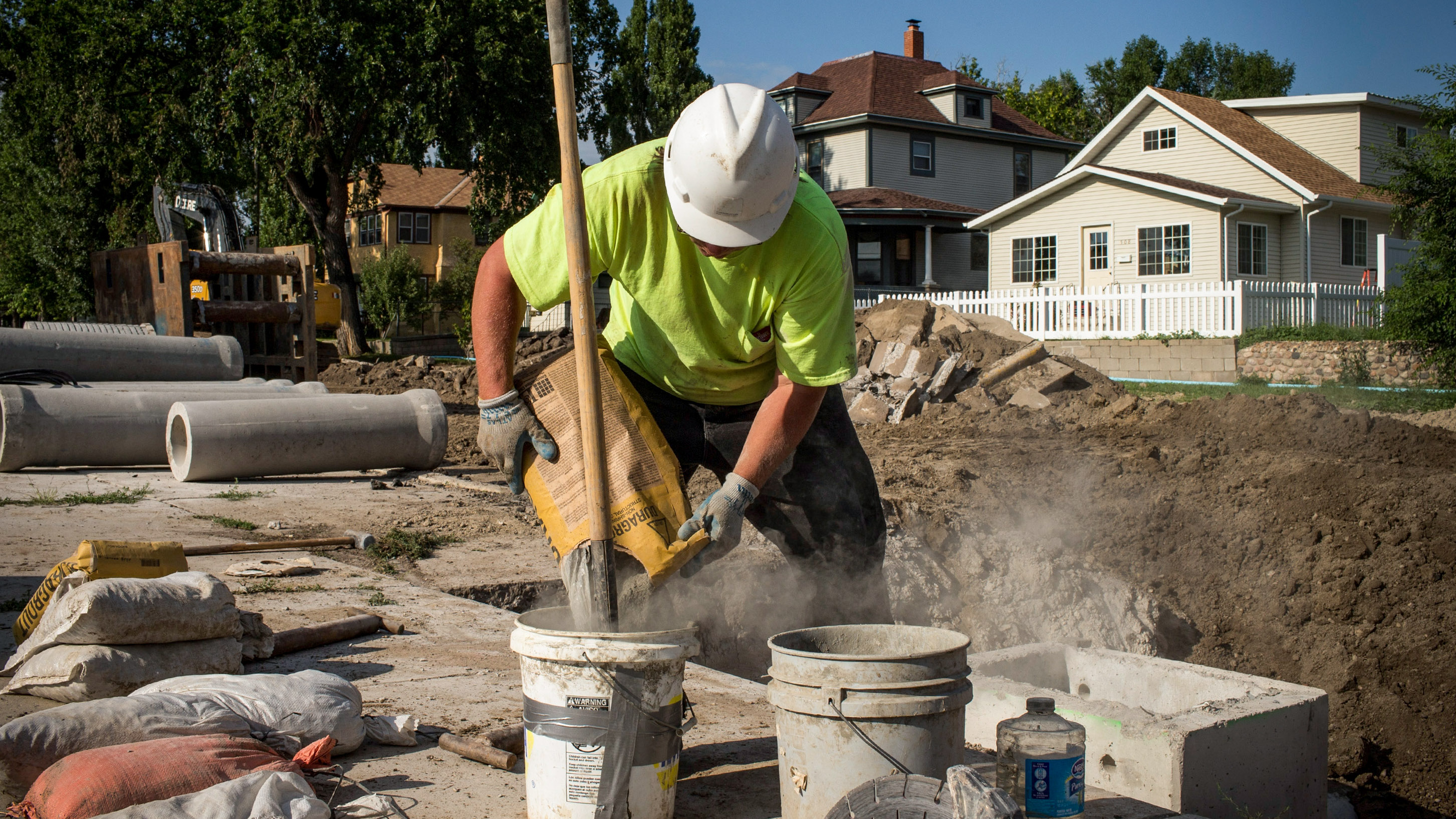 construction worker mixing cement near an open foundation with finished homes visible in the background