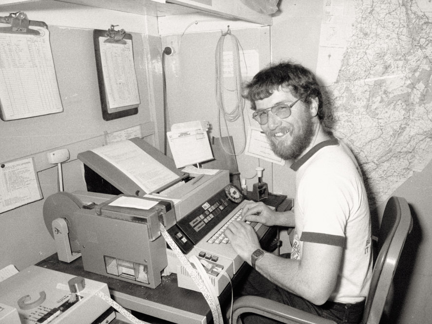 a smiling person in a t-shirt types at a telex