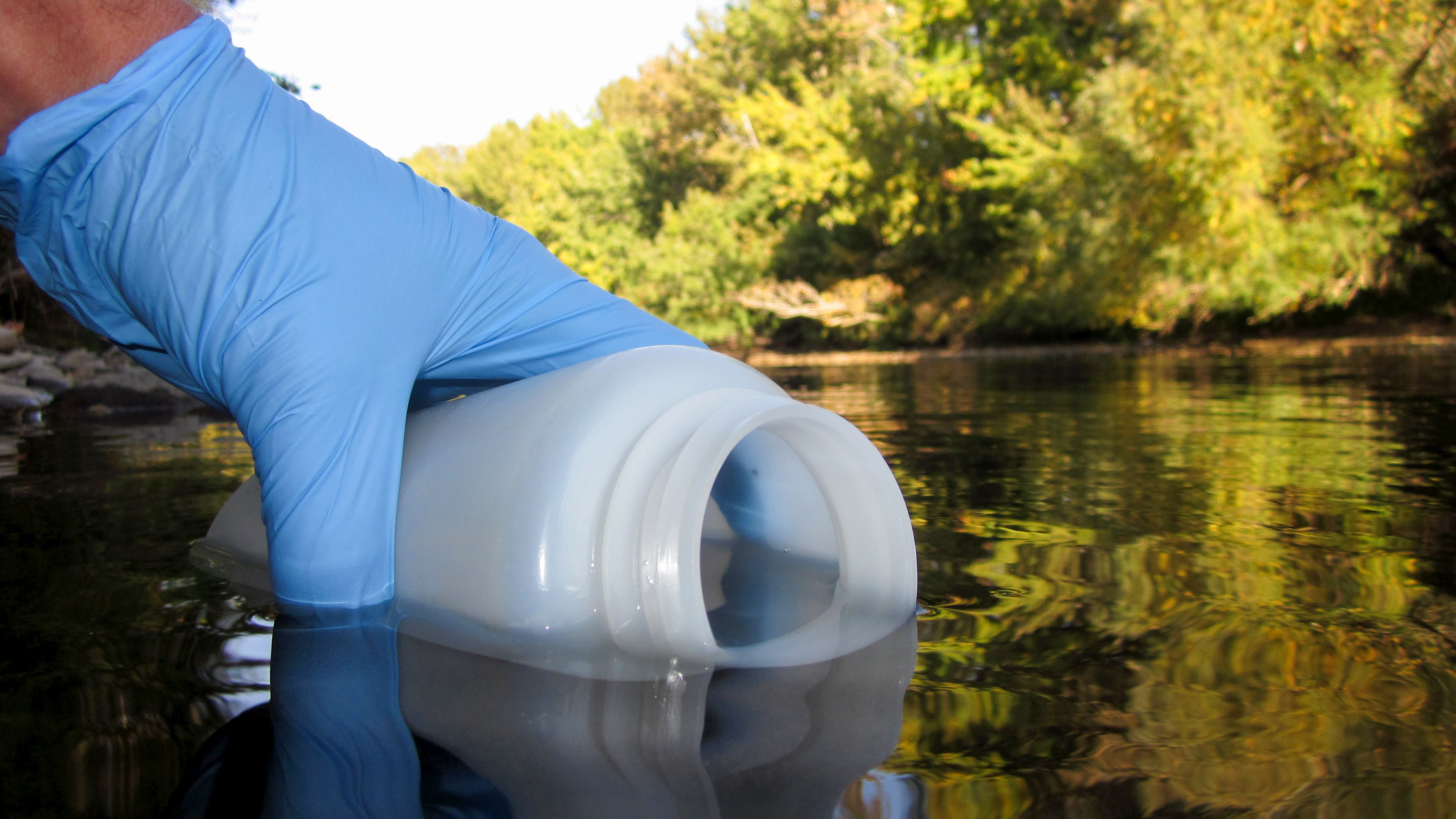 close up of a gloved hand holding a 1-liter bottle to collect an eDNA sample from the Boise River