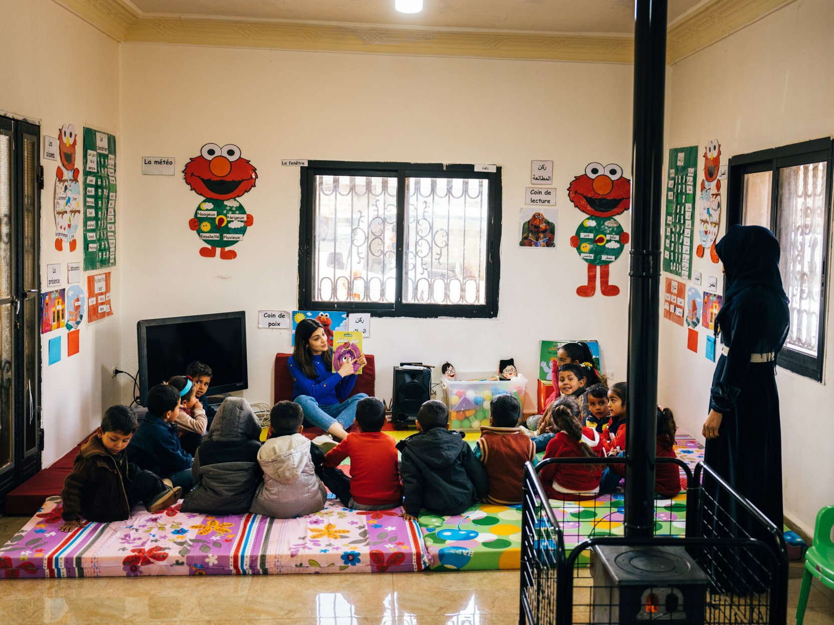 a classroom of children seated on a rug to listen to a story being read by a teacher