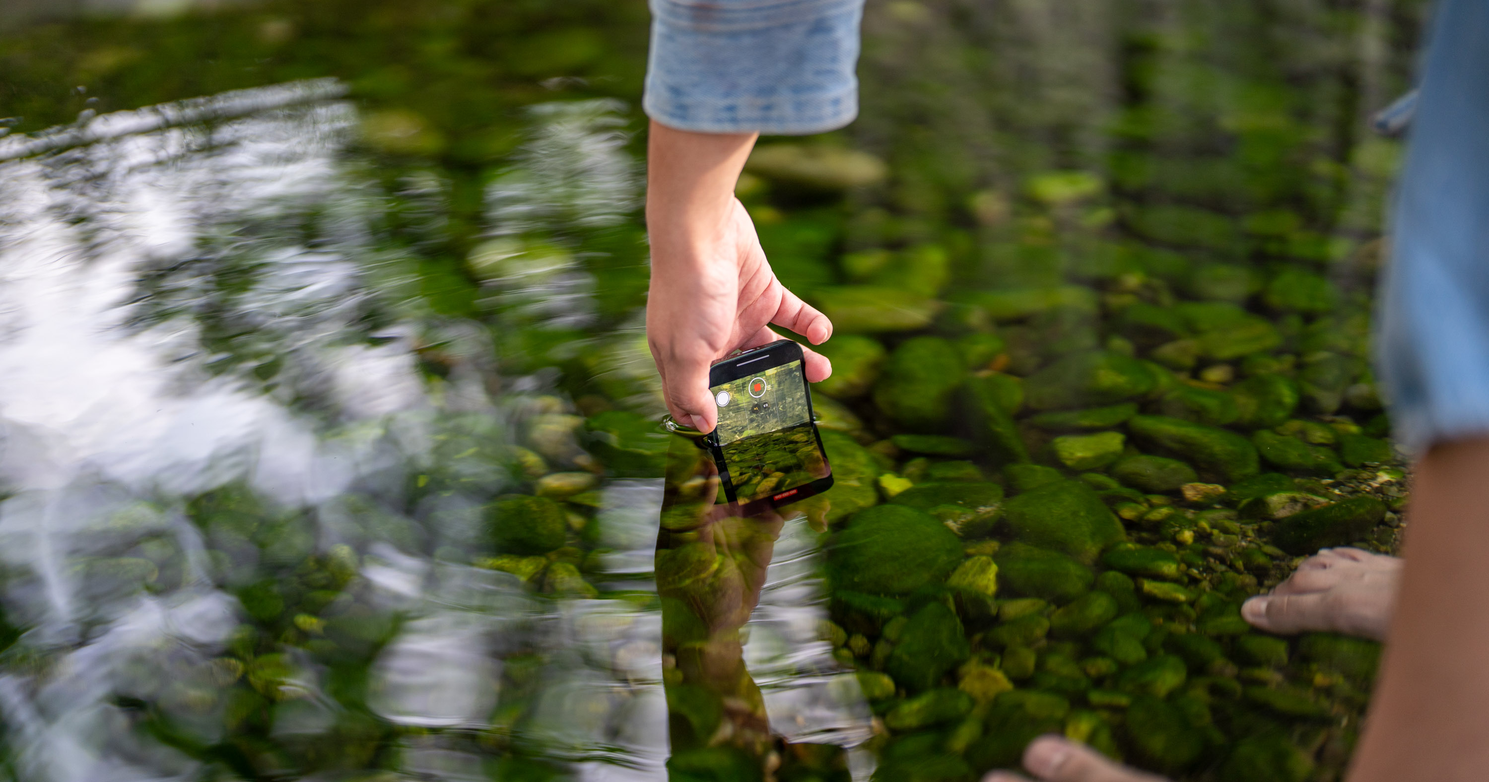 a hand submerging a cell phone into water