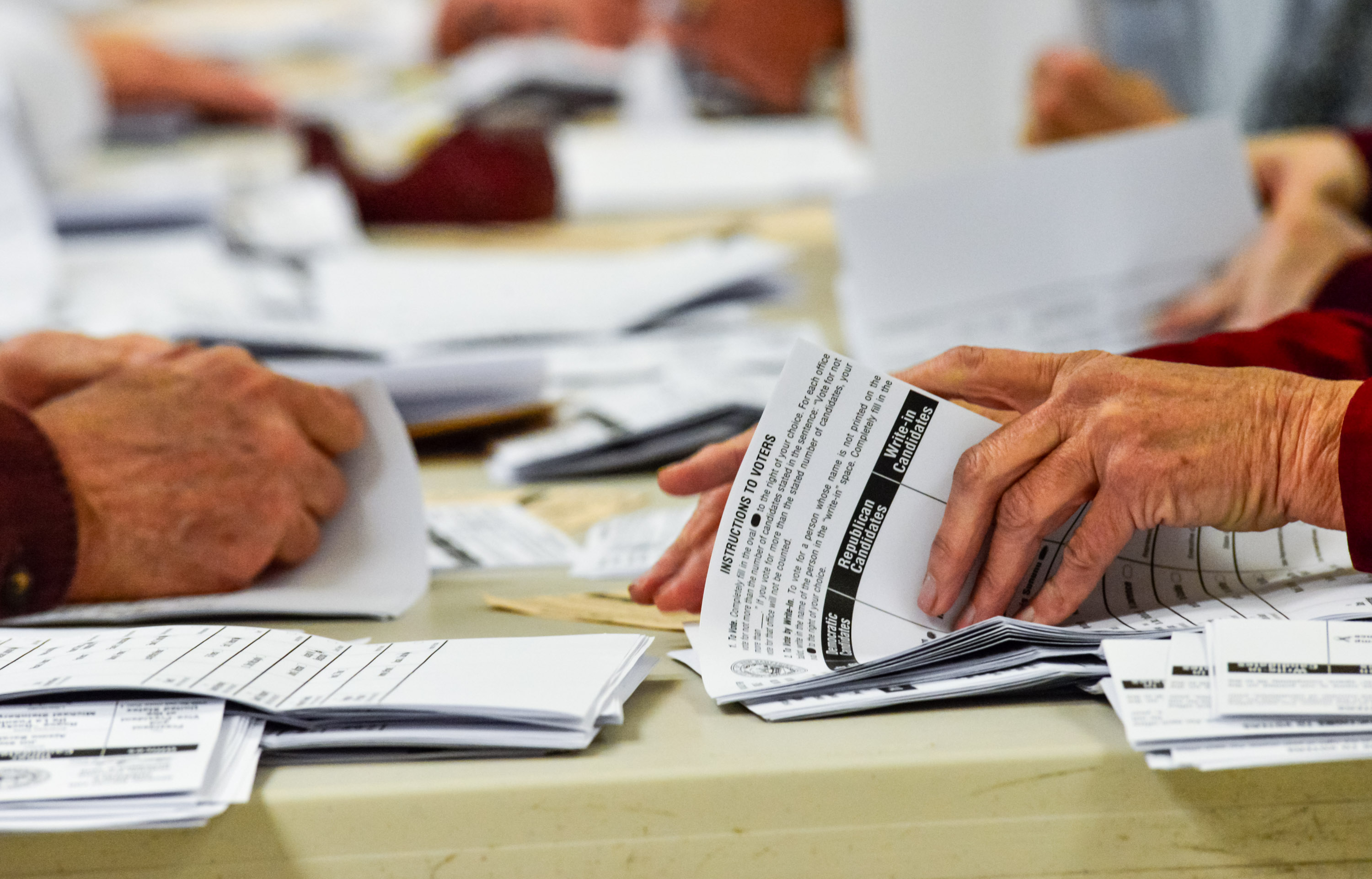 close up view of hands counting stacks of ballots
