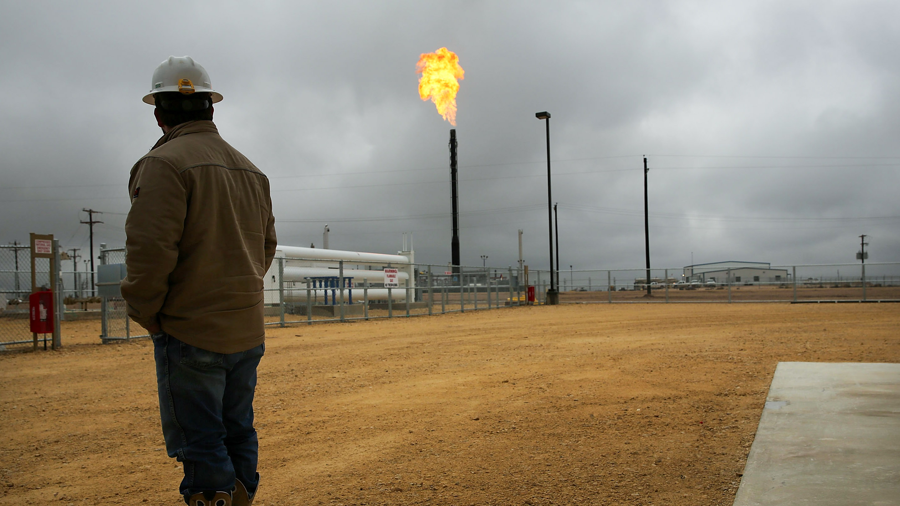 worker in hard hat at the Deadwood natural gas plant looks toward the flared natural gas burning in the distance