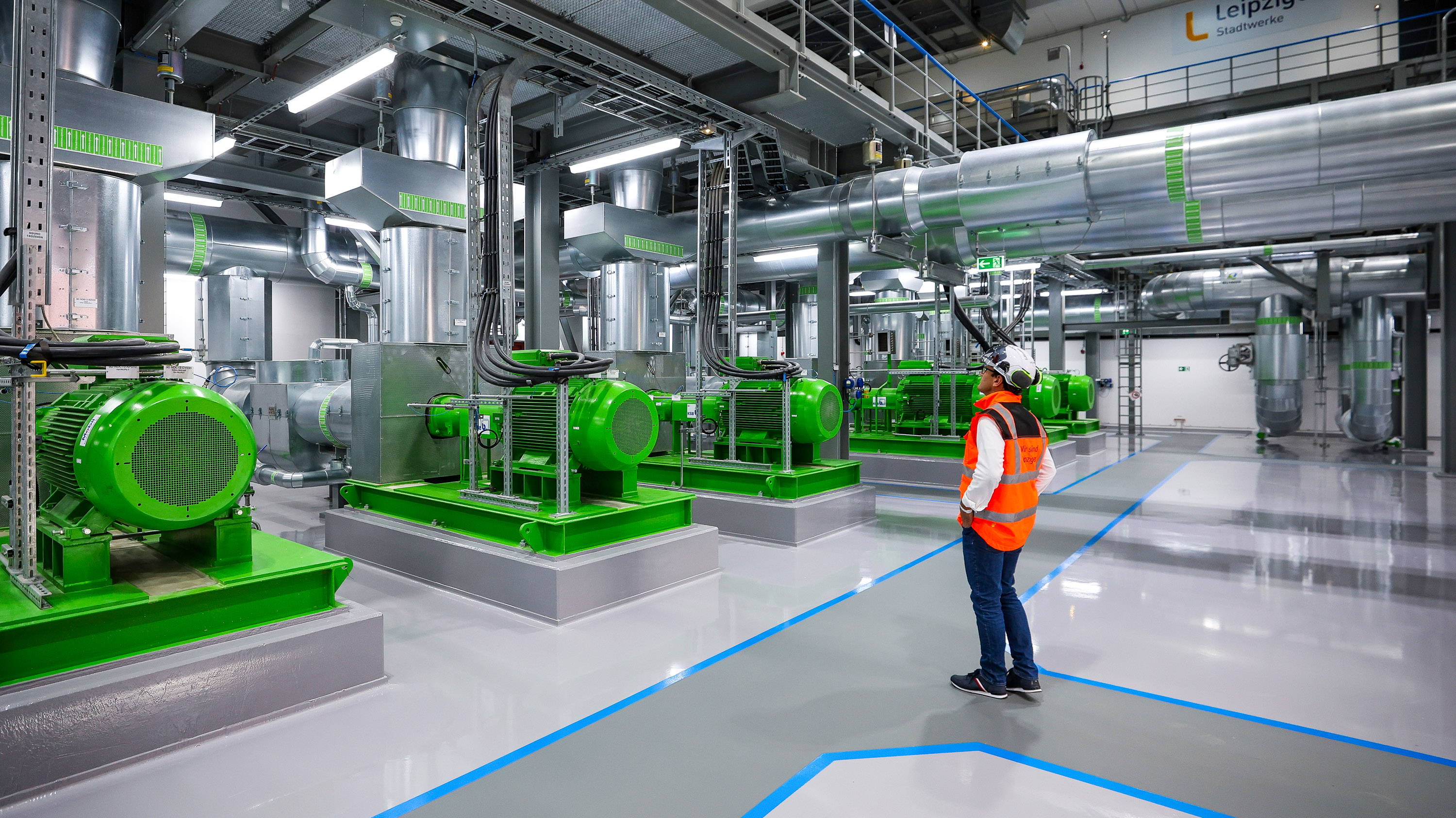 power plant worker stands in front of a row of green pumps