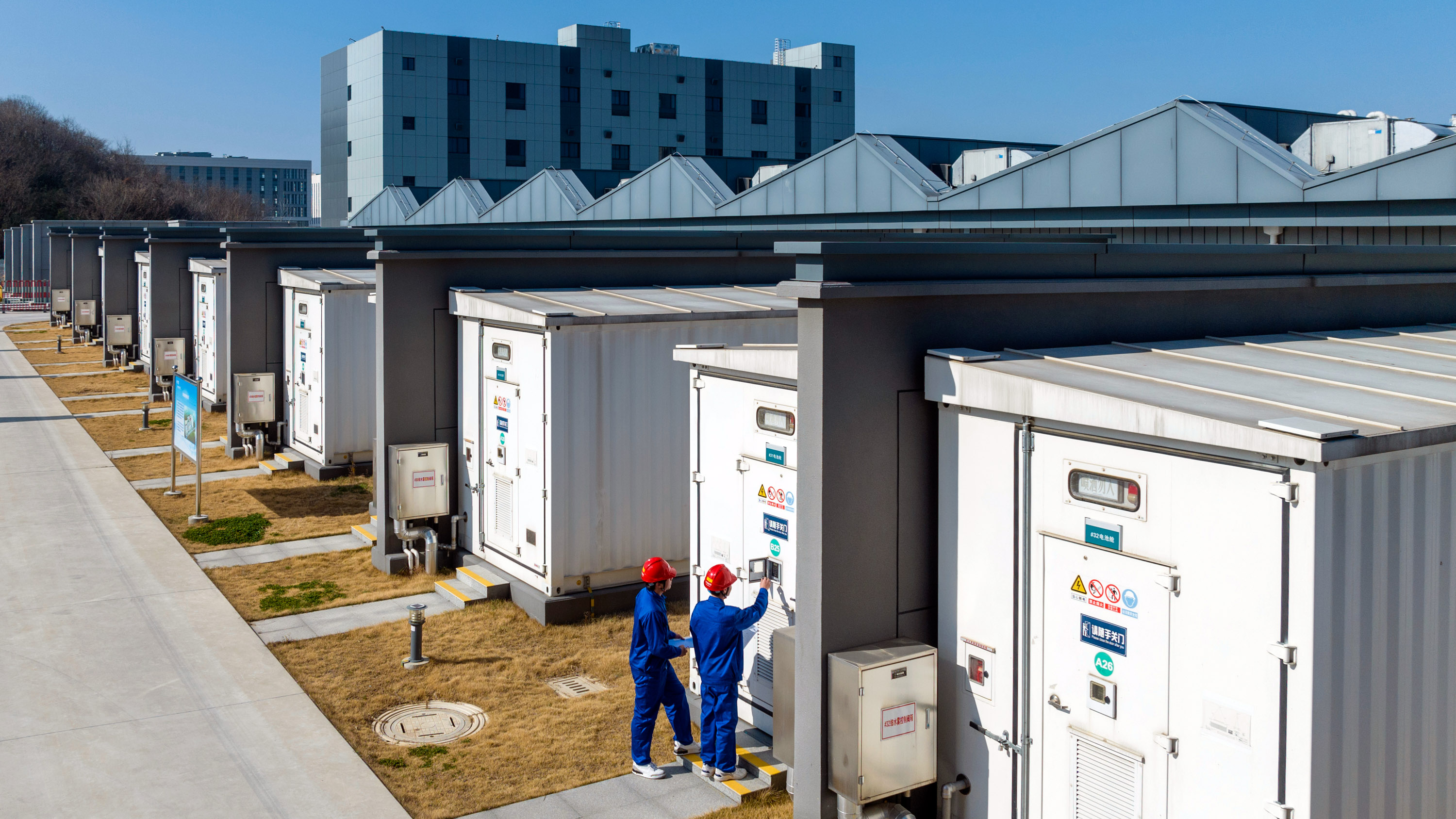 two workers in red hard hats checking a panel of a battery bin at a energy storage power station