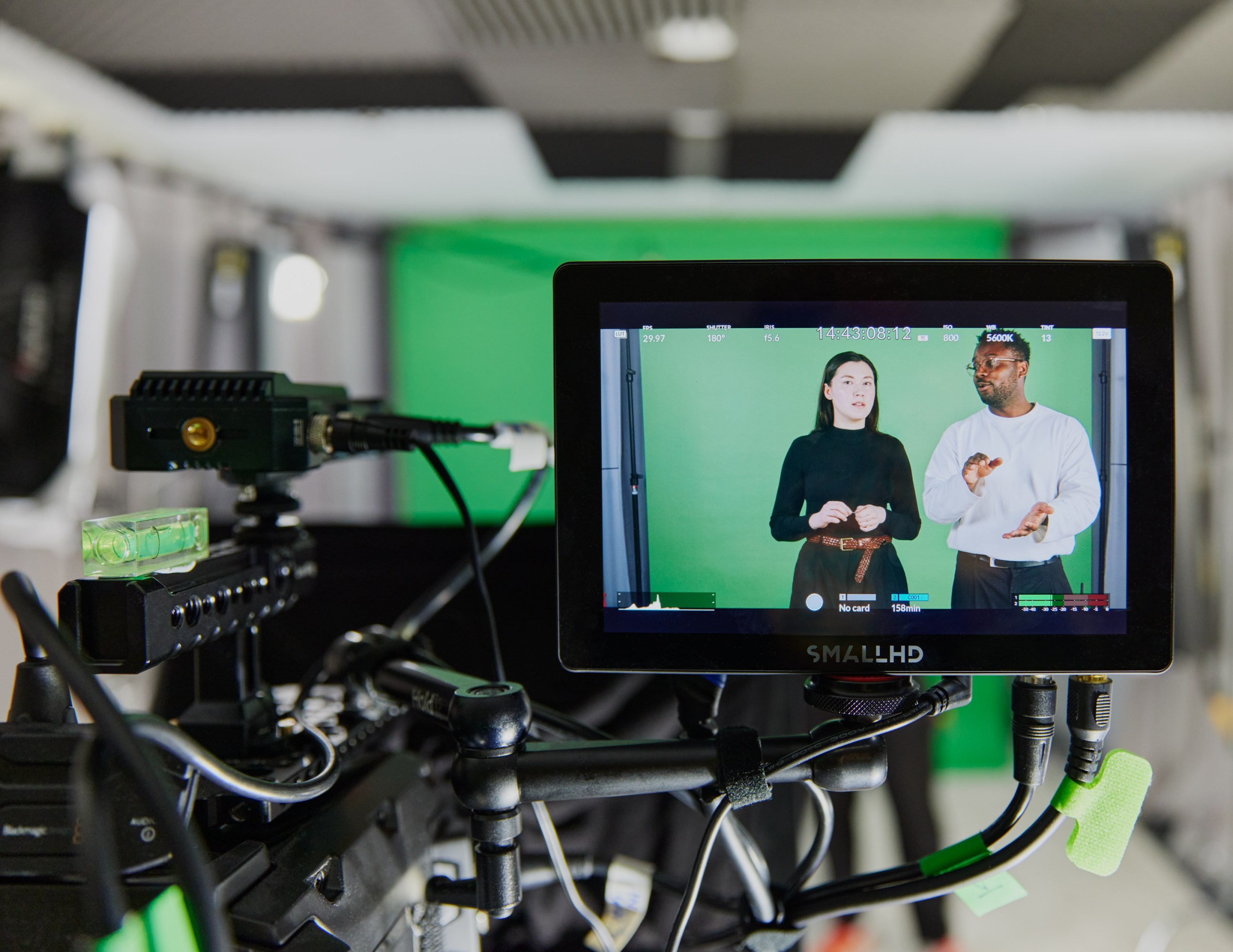 monitor on a video camera showing Heikkilä and Oshinyemi on set in front of the green screen