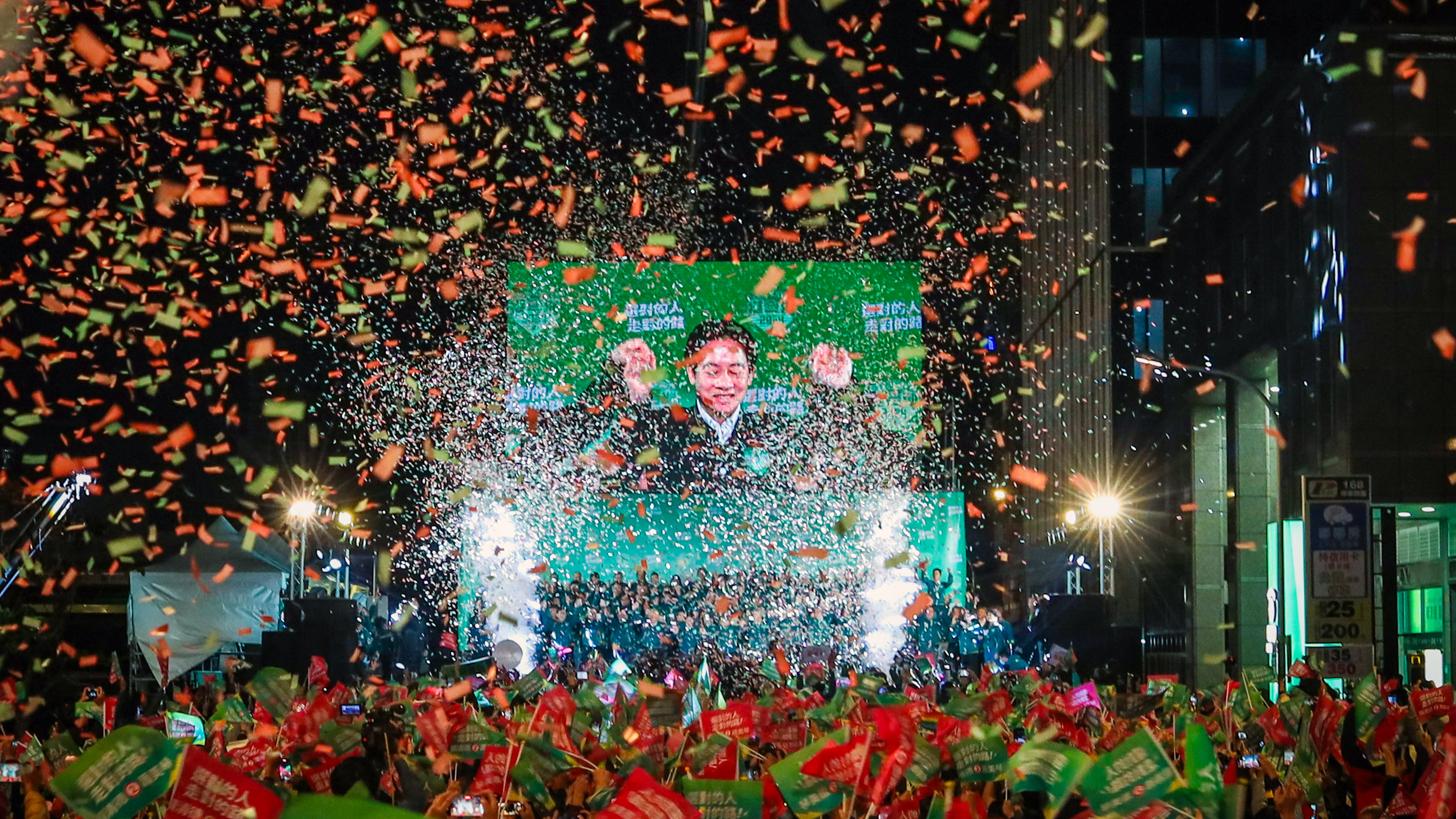 Confetti flies over the stage and crowd at night with president-elect Lai Ching-te on the big screen in the center