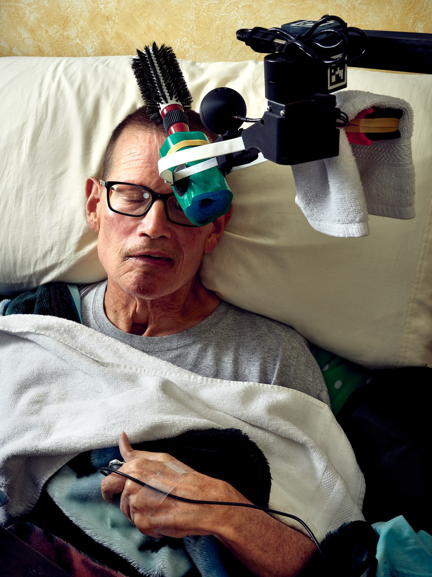 Un brazo robótico sostiene un cepillo sobre la cabeza de Henry Evans, que descansa sobre una almohada.