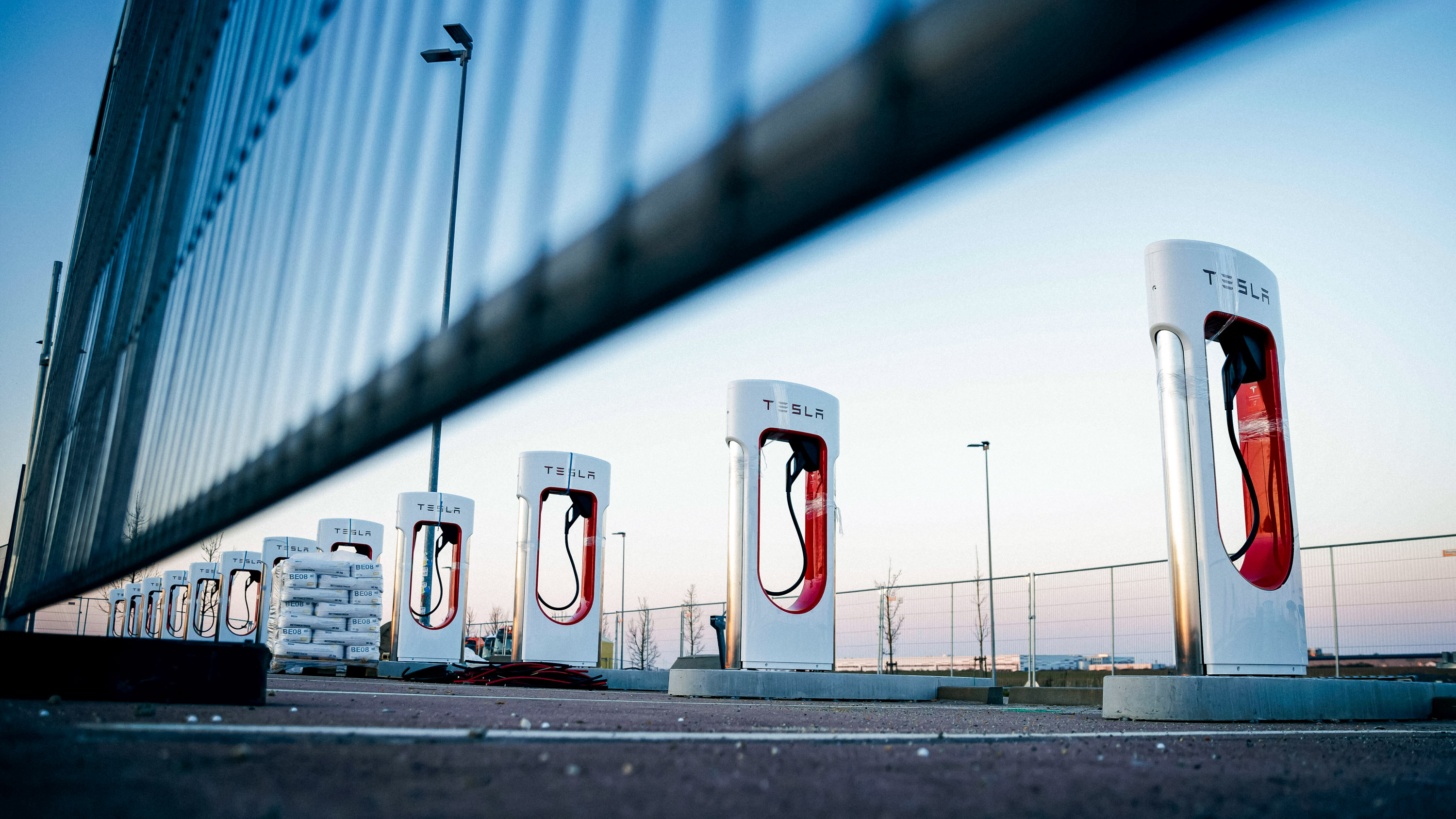 Row of Tesla superchargers seen from a low angle under a barriewr in early morning light