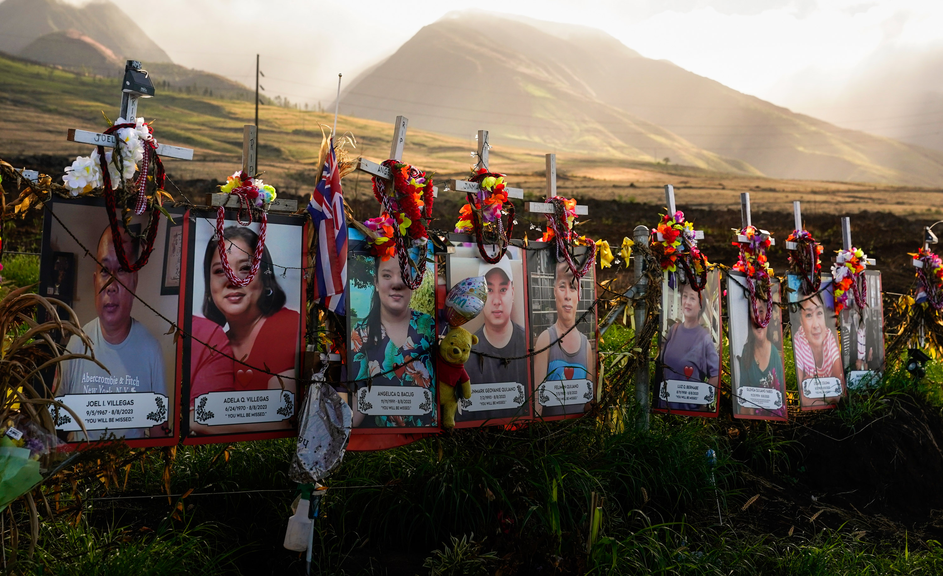 Photos of victims are displayed under white crosses at a memorial for the August 2023 wildfire victims