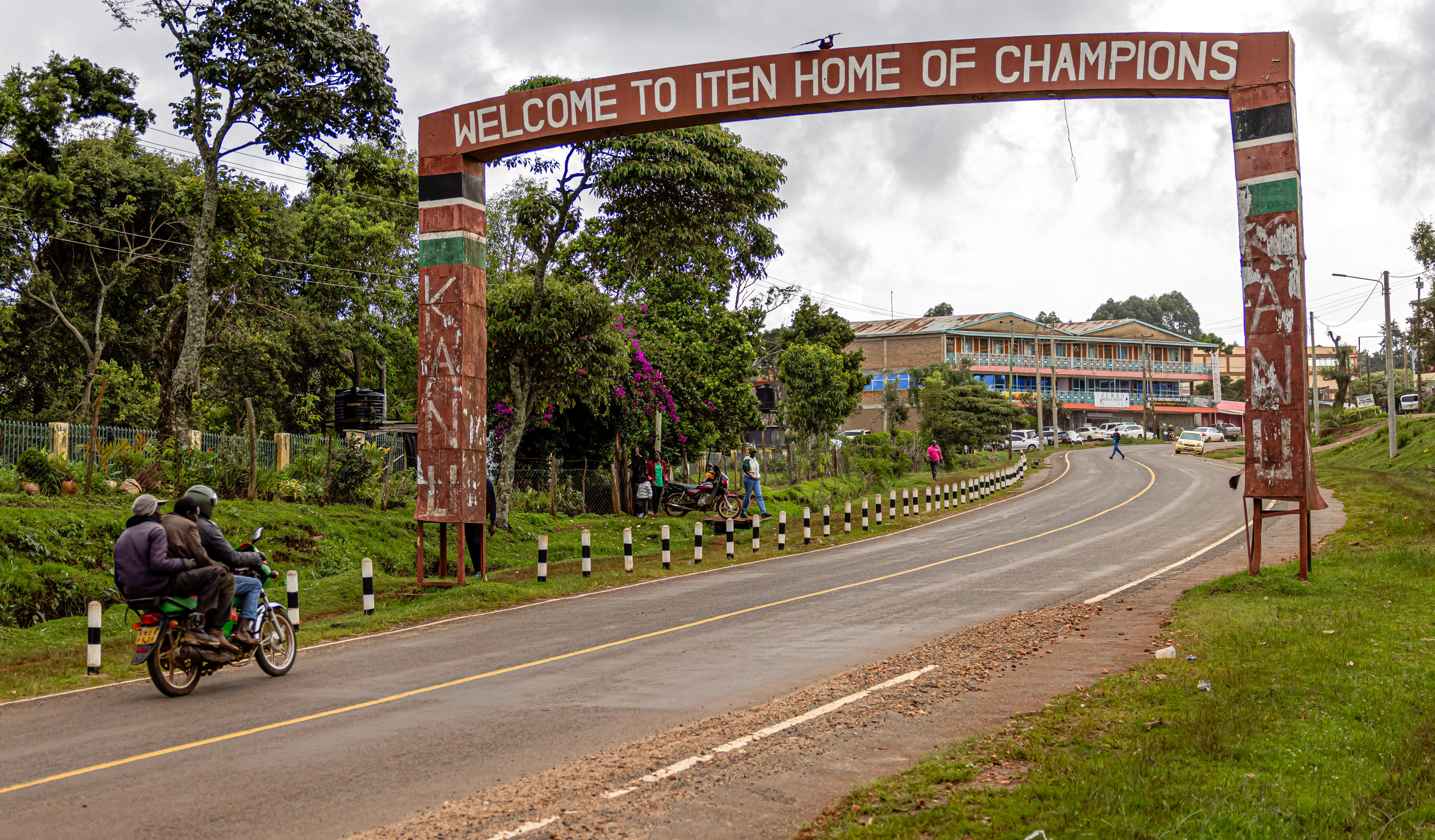 A motorcycle drives past a sign that reads “Welcome to Iten Home of Champions”